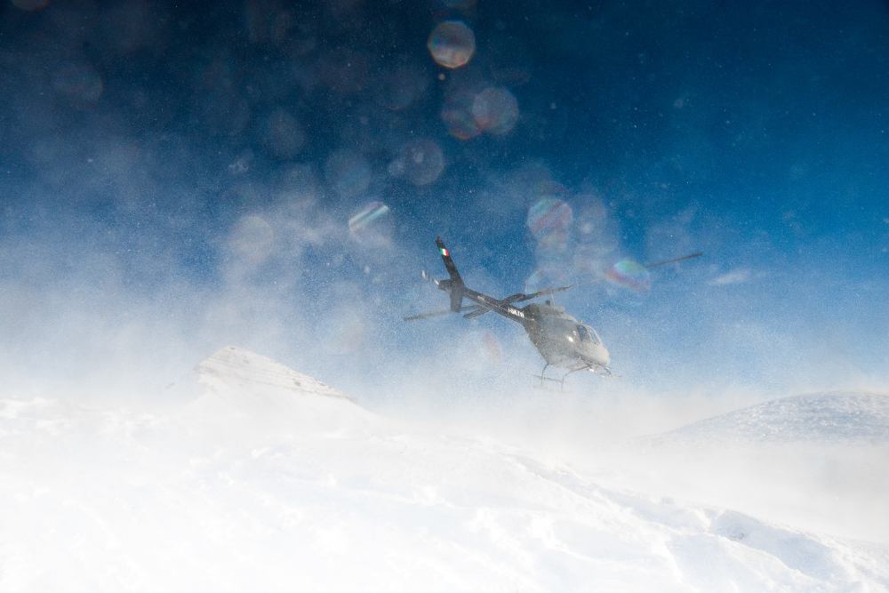 A helicopter flying above a snowy mountaintop, the view obstructed by flying snow