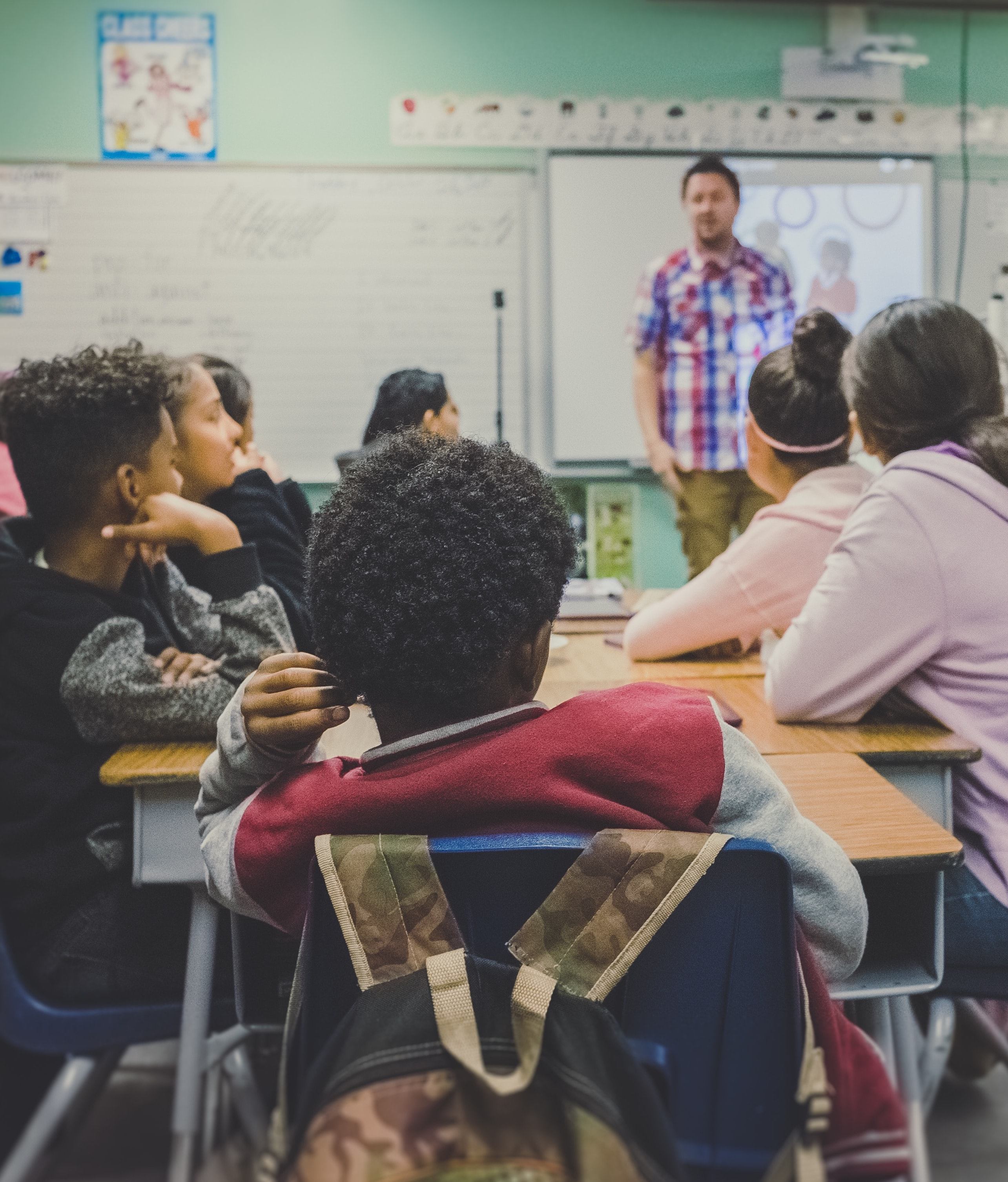 An adult talking to a group of listening students in a middle school classroom